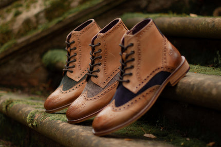 A row of Brogue Gatsby men's boots with heritage tweed propped up against mossy stone steps