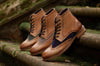 A row of Brogue Gatsby men's boots with heritage tweed propped up against mossy stone steps