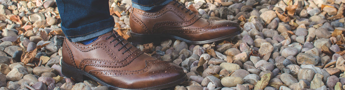 Brown leather brogues worn with navy trousers on a gravel path